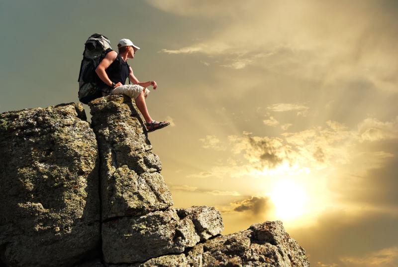 坐在山顶看太阳的登山者