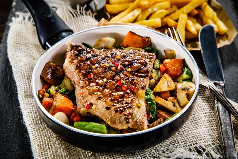 扒牛排配的炸薯条和蔬菜在黑石桌上食用