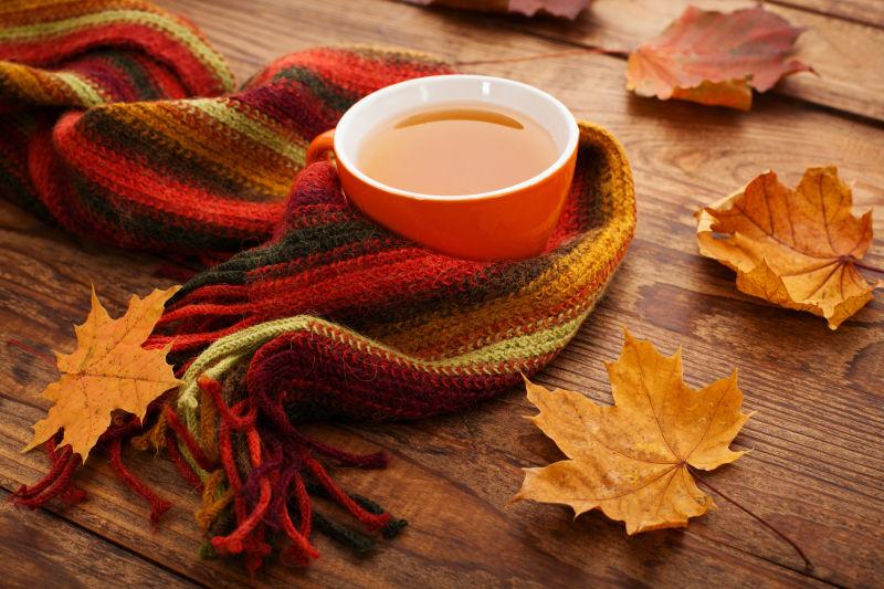 木桌上围巾包裹的咖啡和秋天的落叶