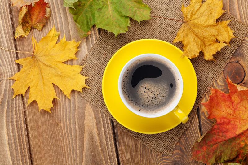 木桌上的一杯咖啡和不同颜色的落叶