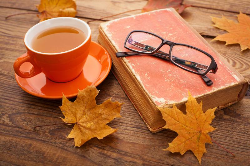 木桌上的一杯咖啡和书眼镜以及漂亮的落叶