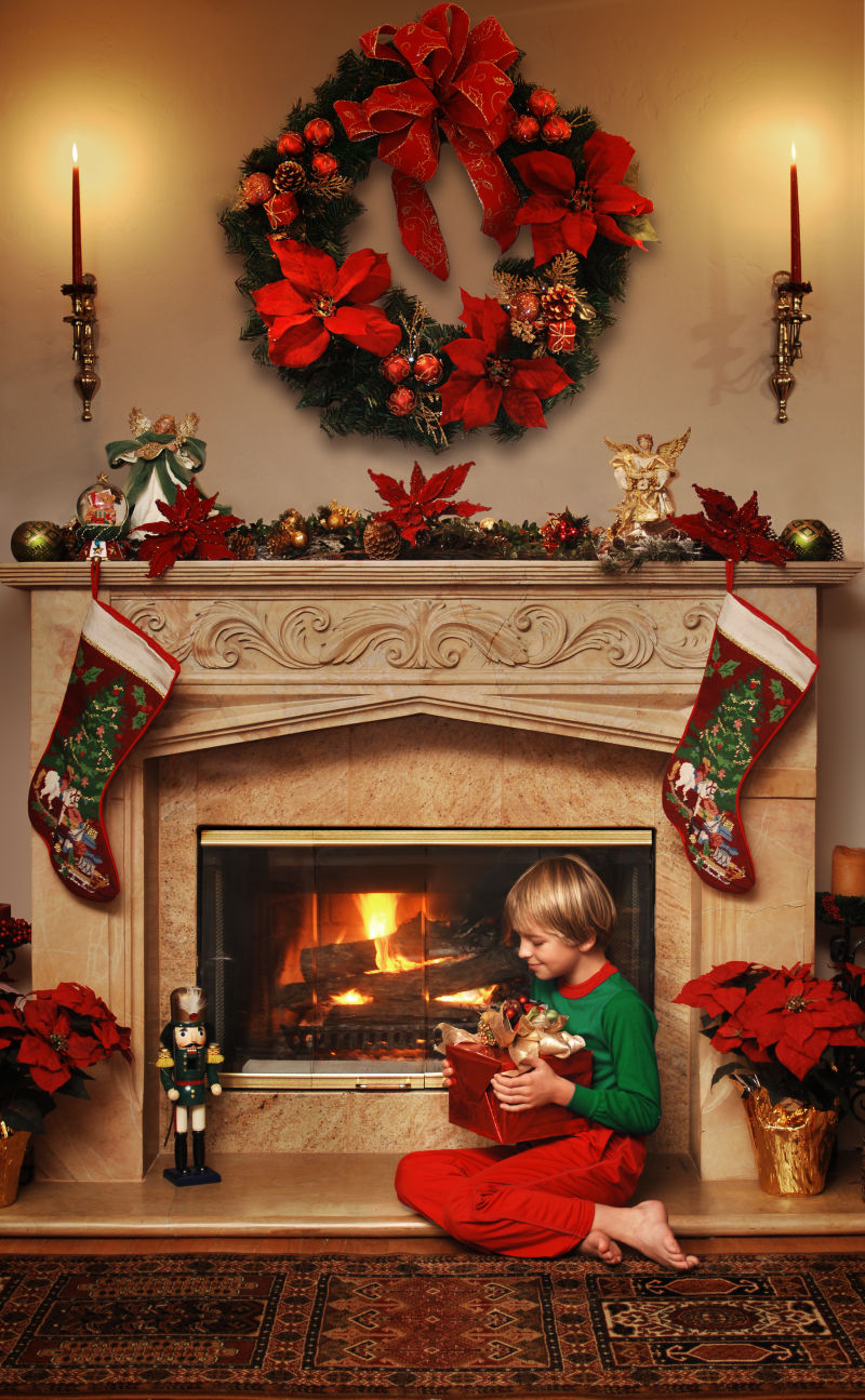 8岁男孩坐在炉火旁拿着圣诞礼物开心的笑