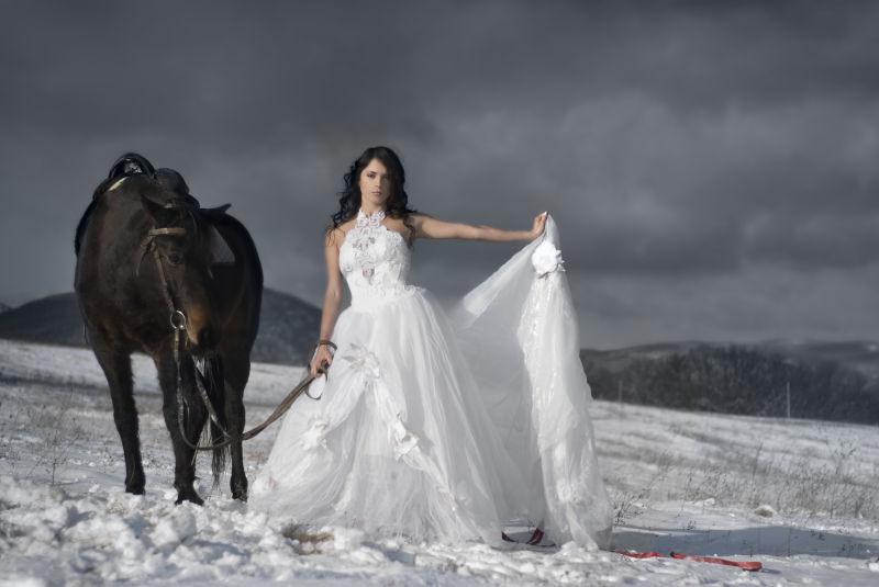 穿白色婚紗牽著馬在雪地裡的美女