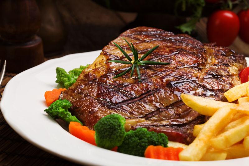 放在白色盘子里的扒牛排配炸薯条和蔬菜