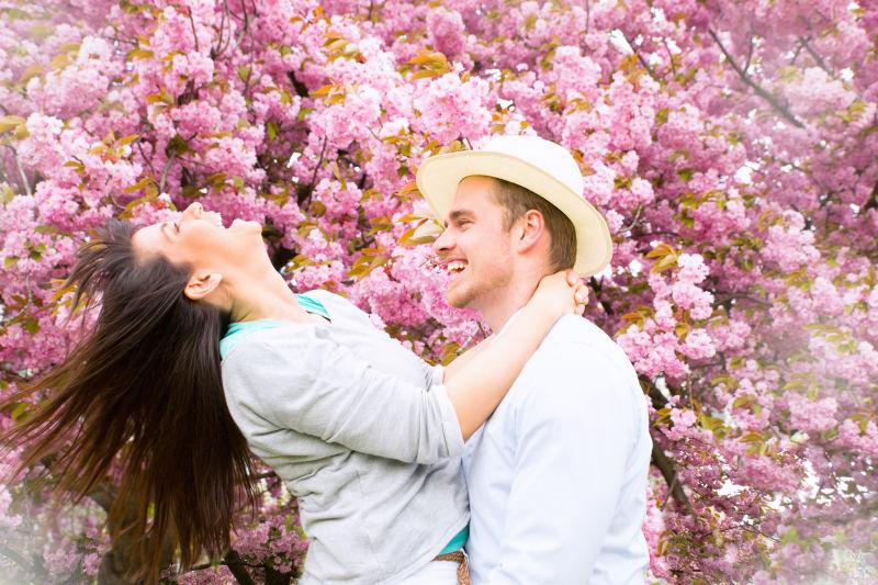 在开花的树旁边的开心的情侣