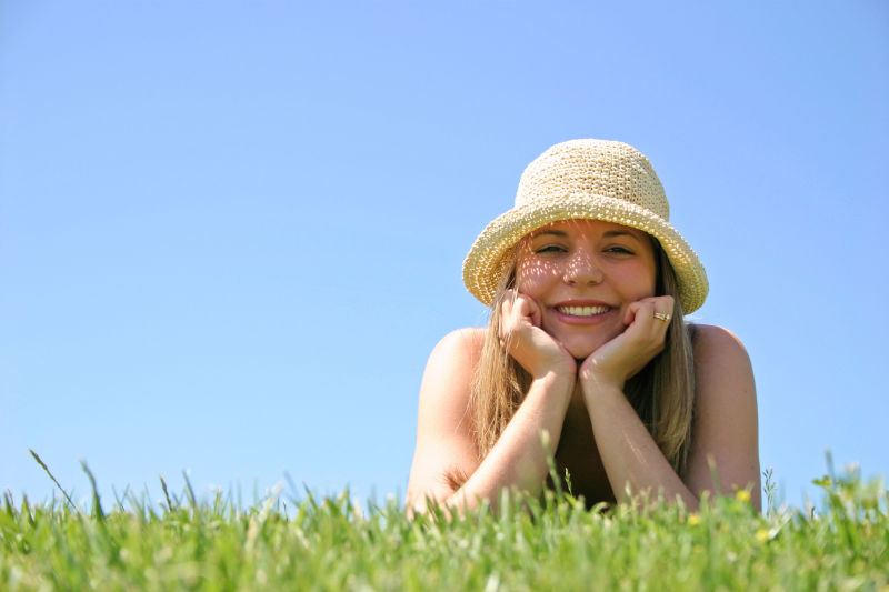 蓝天下微笑的美女趴在草地上