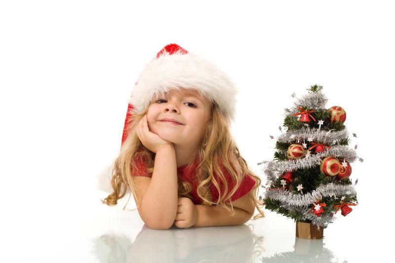 白色背景上的戴着圣诞帽的小女孩和圣诞树