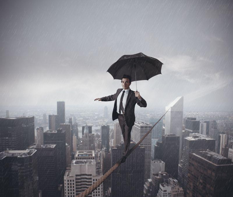 打着伞走在城市摩天大楼之间绳子上的男商人