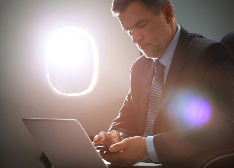 坐在飞机上的笔记本电脑前的商人