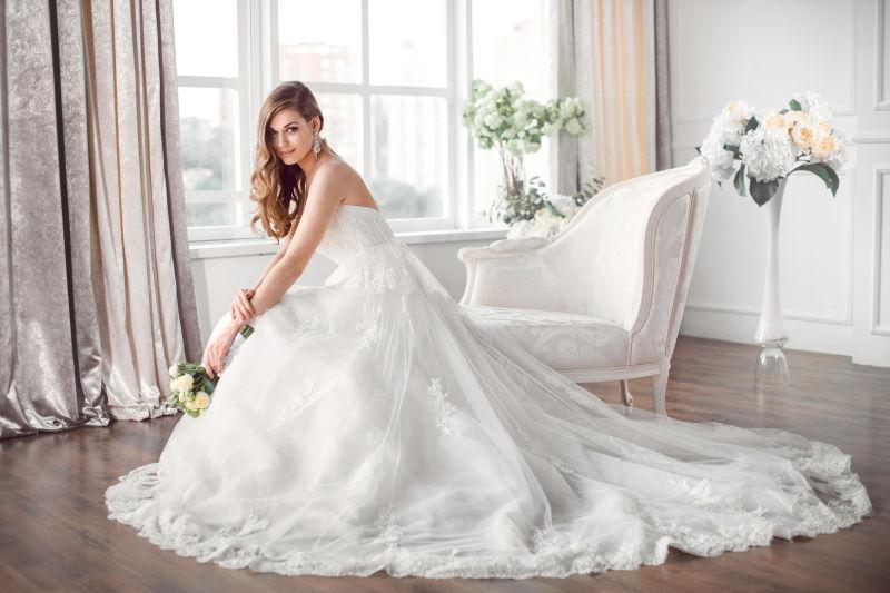 新娘穿着漂亮的衣服坐在室内的白色沙发上
