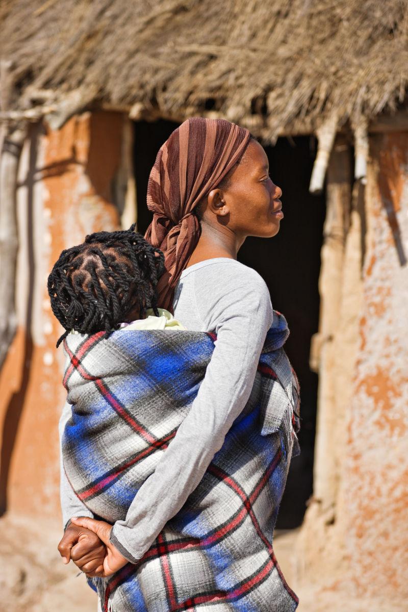 非洲母亲在小屋前以传统的方式带孩子