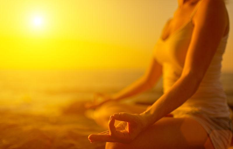 日落时沙滩上瑜伽姿势冥想的美女