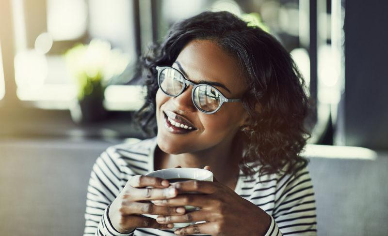 微笑的非洲年轻女子在咖啡馆喝咖啡