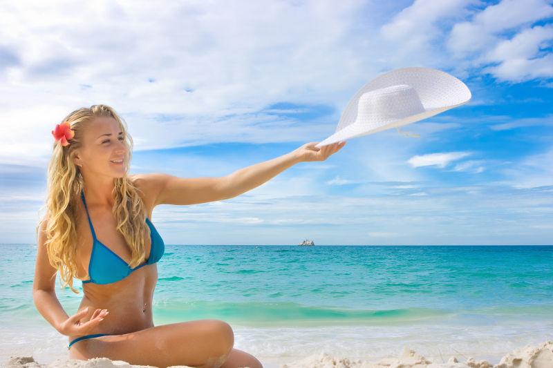 海滩上拿着白色太阳帽的比基尼女孩