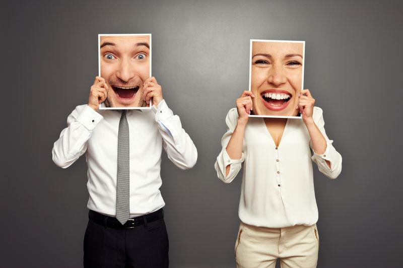 灰色背景中举着微笑框架的男人和女人