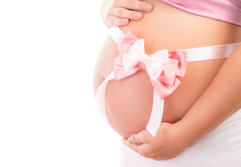 白色背景下孕妇大肚子上粉红色的蝴蝶结