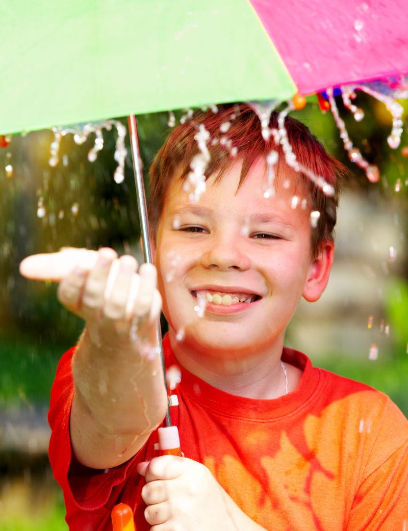 雨伞下伸出手接水的孩子
