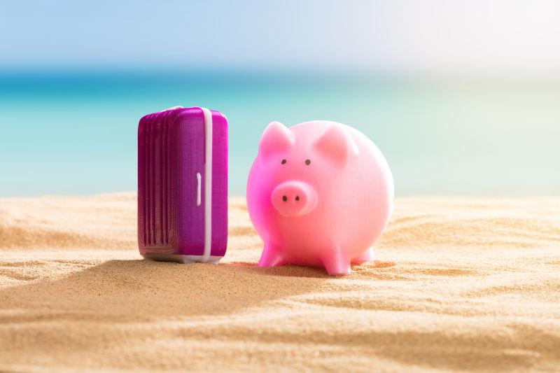 沙滩上的一个小猪存钱罐和行李箱