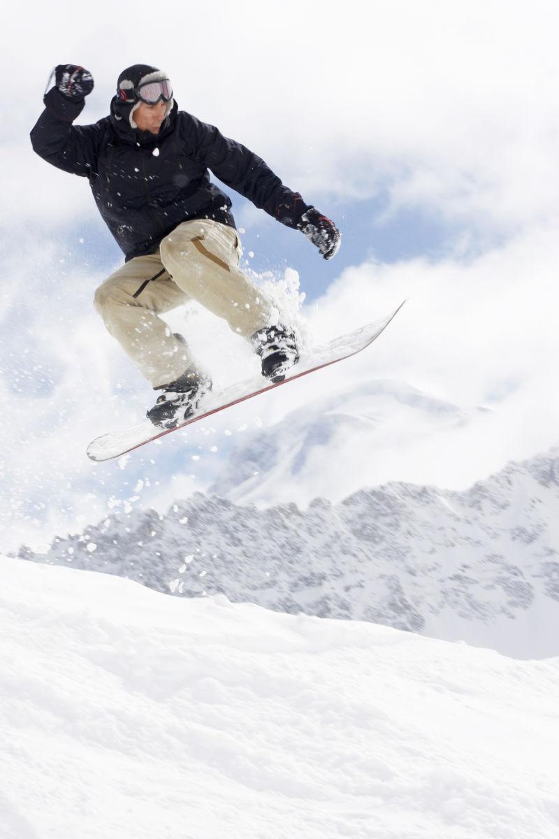 白色雪山背景上跳起来的单板滑雪者