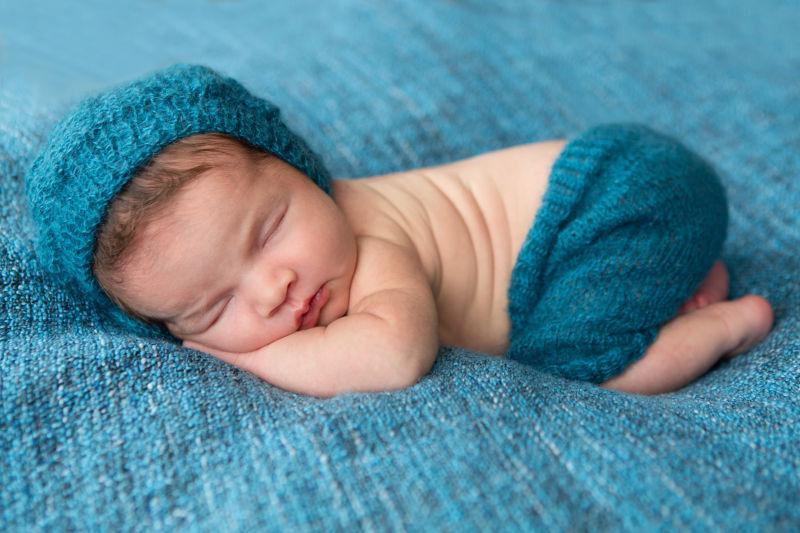 蓝色背景中带着针织帽趴着睡觉的新生儿