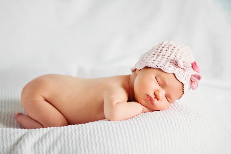 白色背景中带着帽子趴着睡觉的新生儿