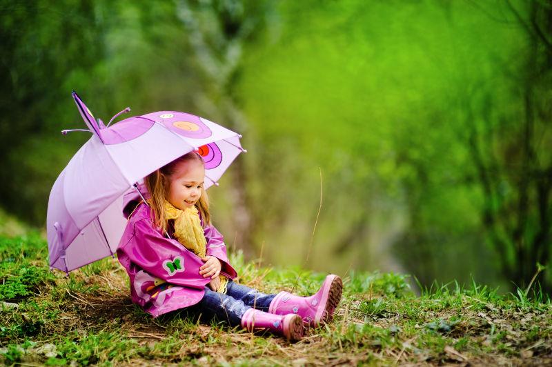 绿色户外背景下带着雨伞和靴子的小女孩