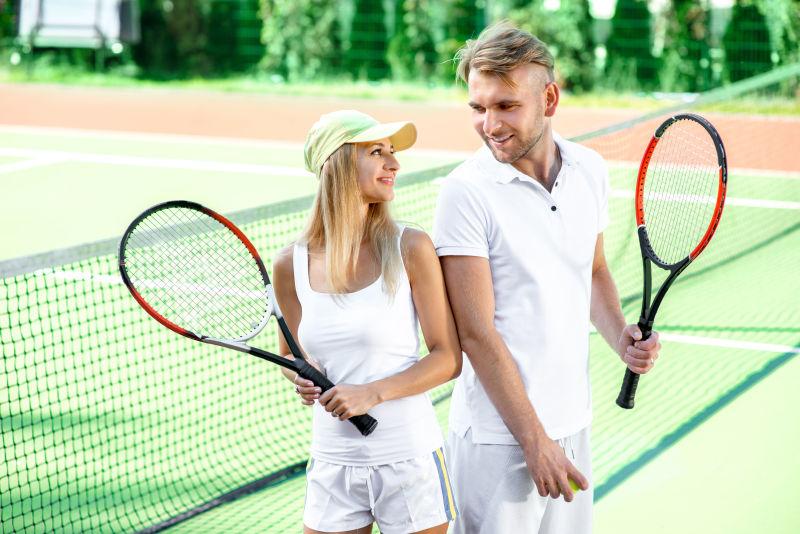 年轻夫妇在夏天外面的网球场上打网球