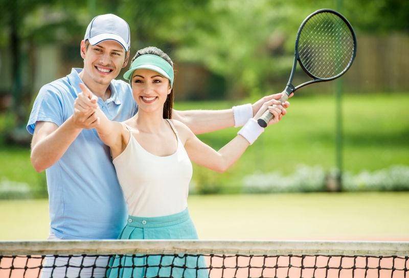 微笑着的年轻夫妇站在网球场上