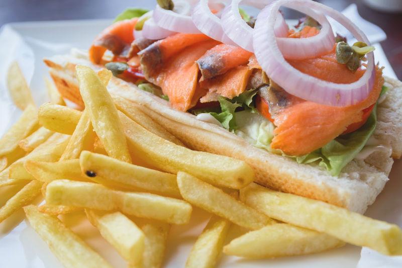 白色餐盘里的薯条洋葱和鱼片的三明治