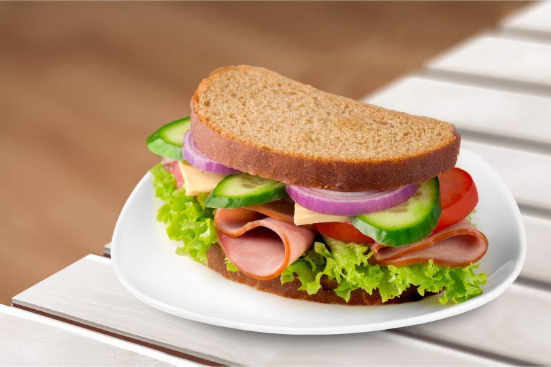 放在白色桌子上的夹着黄瓜西红柿生菜火腿的三明治
