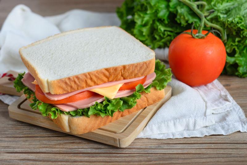 放在木质砧板上的美味的夹着火腿奶酪和生菜的三明治