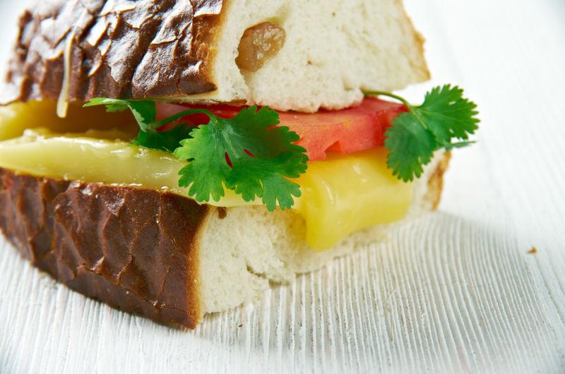 白色木桌上夹着奶酪和西红柿的三明治