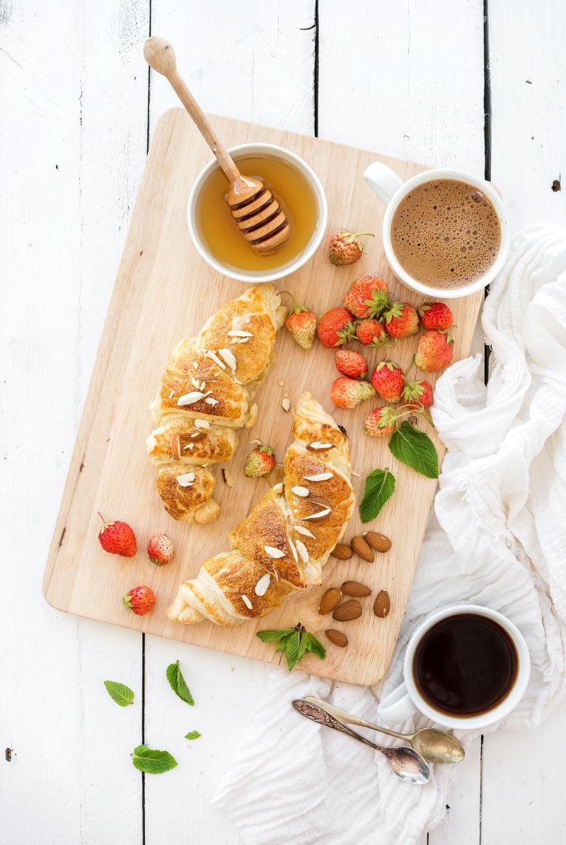 在服务板上的白色乡村木材背景上的新鲜烤杏仁羊角面包