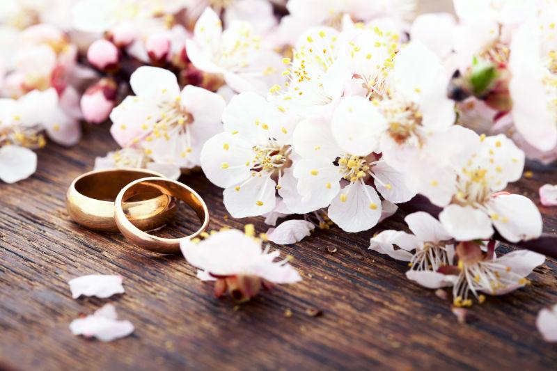木桌上粉色桃花旁的金色结婚戒指