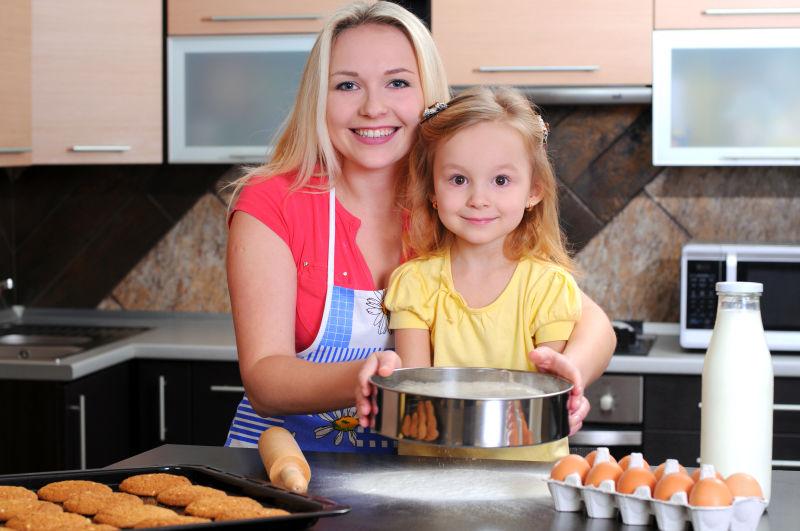 厨房背景中教给女儿做烘焙的母亲