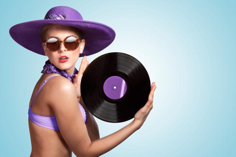 性感的女人戴着帽子与太阳镜拿着一张唱片