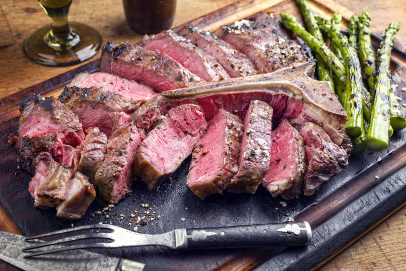 烤肉和牛排切片干燥老化与绿芦笋上砧板