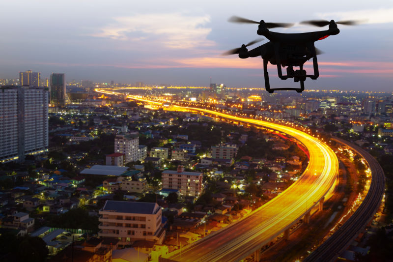日落时无人驾驶飞机在城市上空飞行的剪影