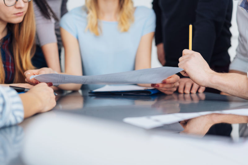 一群在设计工作室工作的人-在桌面和手的低角度视图中-就一张大纸上的设计进行咨询