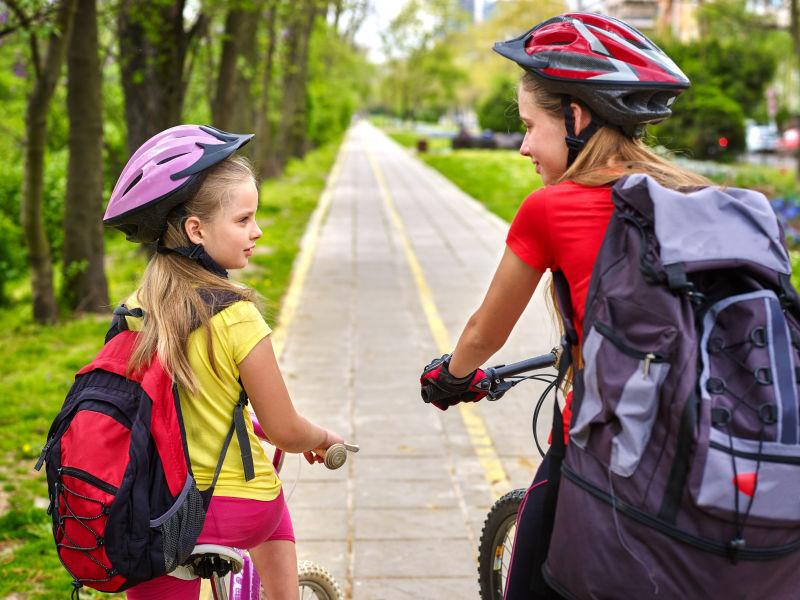 骑自行车的女孩女孩们戴着自行车头盔和玻璃背着帆布包骑着自行车女童在黄色自行车道上骑车自行车共享计划节省了城市街道的金钱和时间儿童