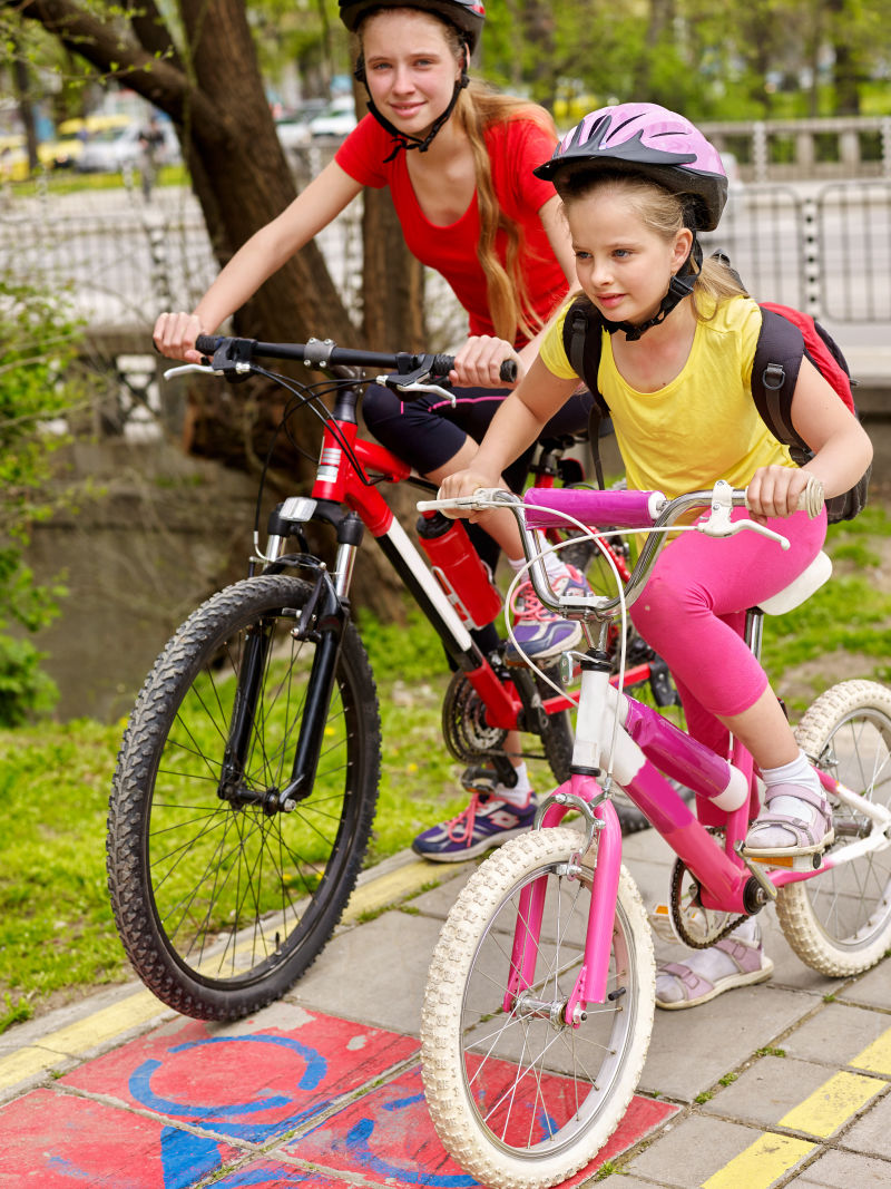 骑自行车的女孩女孩们戴着自行车头盔背着帆布包骑着自行车女童在黄色自行车道上骑车自行车共享计划节省金钱和时间前景中的孩子