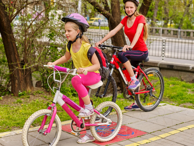骑自行车的女孩两个姐妹戴着自行车头盔背着帆布包的自行车女孩们在黄色自行车道上骑车自行车共享计划节省了城市街道的金钱和时间夏天户外