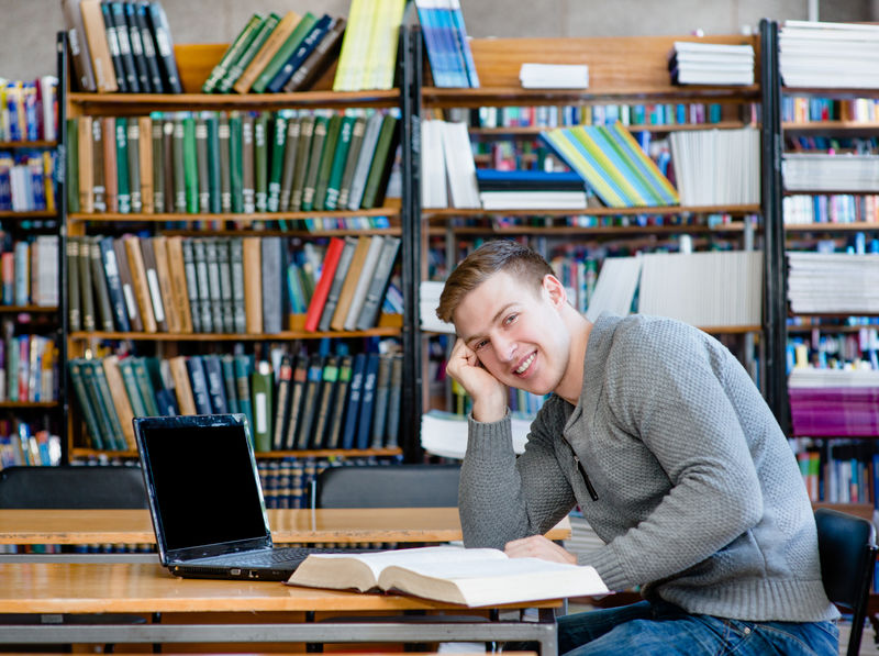 大学图书馆里一个带笔记本电脑的快乐学生的画像