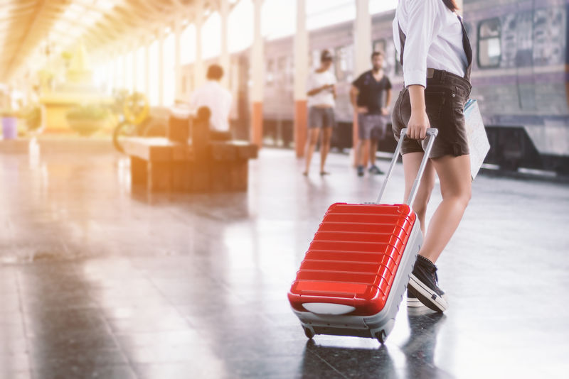 特写镜头中的年轻女旅行者带着她的红色手推车包和地图在火车站