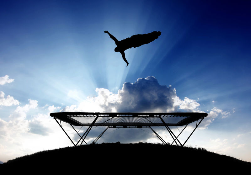 日落时蹦床上的体操运动员孤立的蓝色的