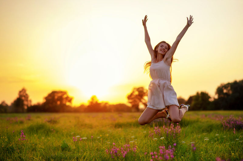 快乐快乐的女孩在夏日日落的背景下跳上大自然