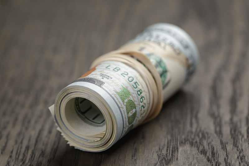 木制桌子上的一卷百美元钞票