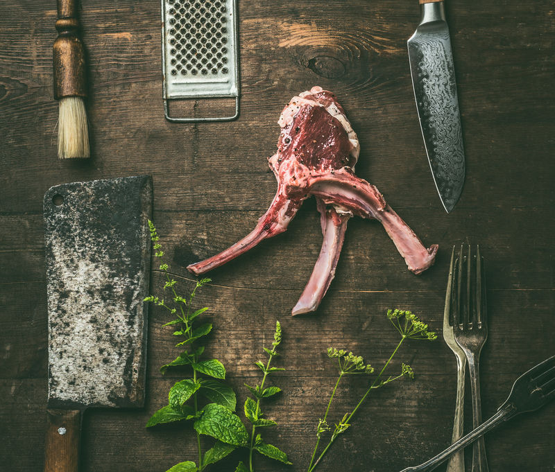 新鲜香草的生羊排和乡村木质背景的厨房用具俯视图烤肉或烧烤准备羊肉架