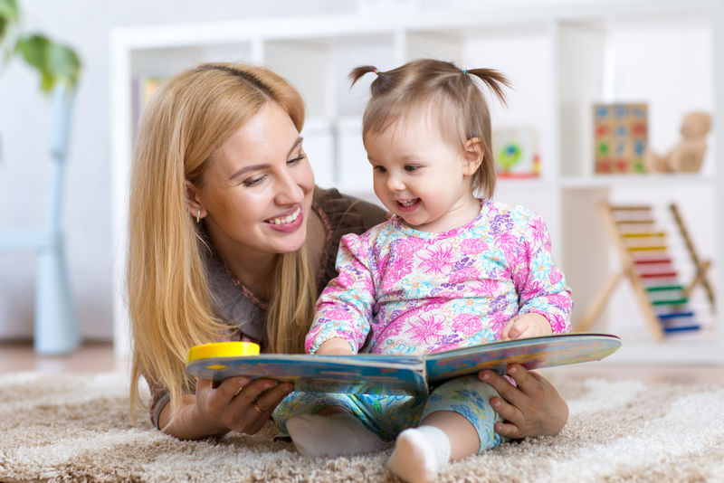 快乐的母亲在室内给女童看书