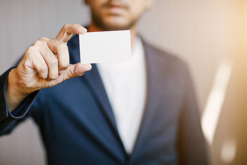 男子持白色名片-男子身穿蓝色衬衫-并展示空白白色名片-背景模糊-横向模仿-聪明亚洲商人职业生涯愉快